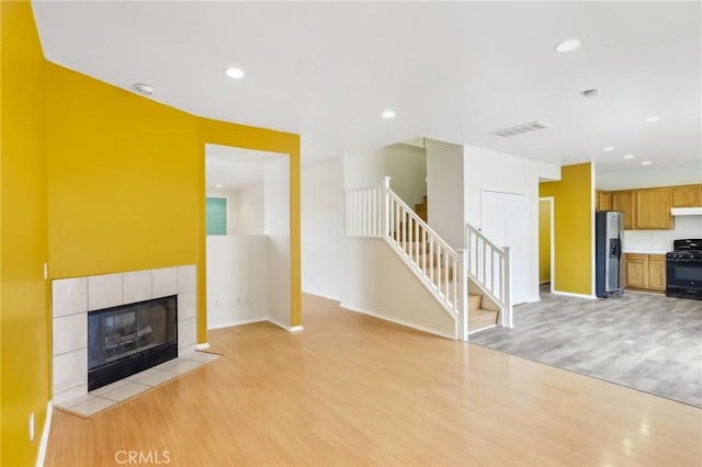 unfurnished living room with light wood finished floors, visible vents, stairway, recessed lighting, and a tile fireplace