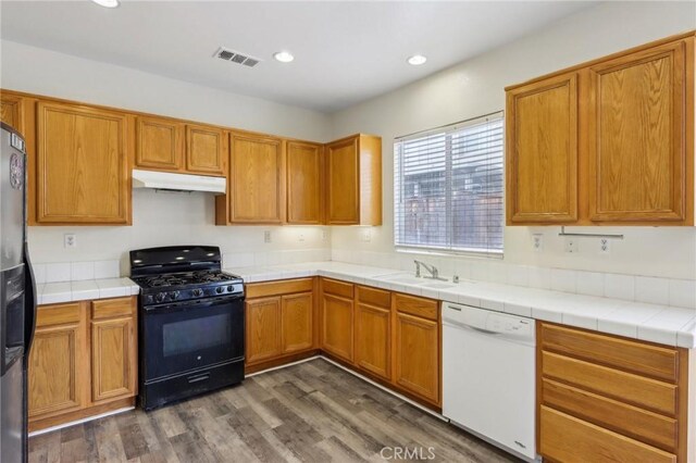 kitchen with white dishwasher, a sink, dark wood-type flooring, black range with gas cooktop, and under cabinet range hood