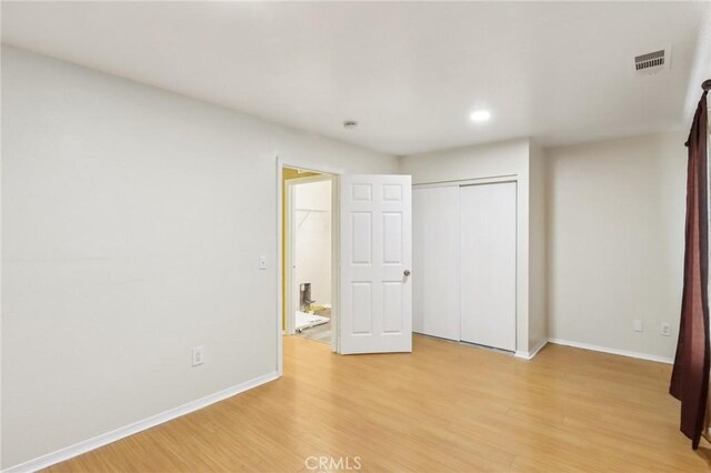 unfurnished bedroom with a closet, visible vents, light wood-style flooring, and baseboards