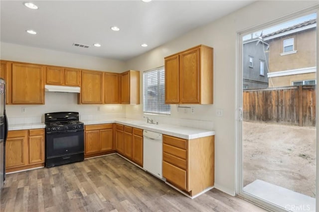 kitchen with black gas range oven, visible vents, under cabinet range hood, tile countertops, and dishwasher