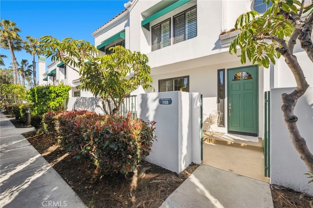 view of exterior entry with stucco siding and fence