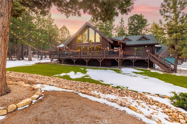 back of house at dusk with log siding, a lawn, and a wooden deck