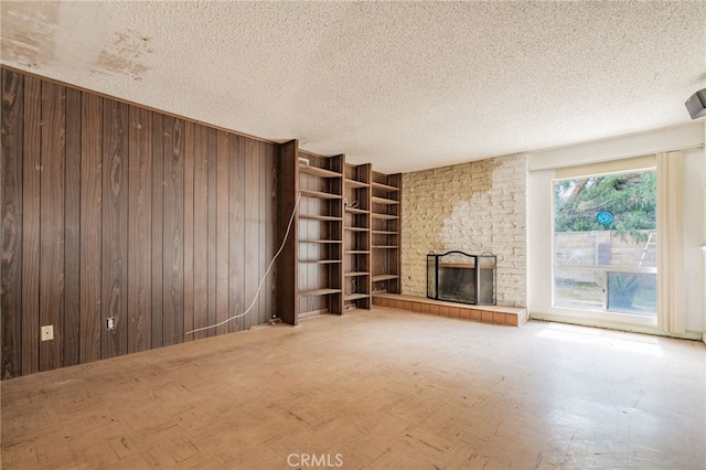 unfurnished living room with wood walls, a brick fireplace, and a textured ceiling