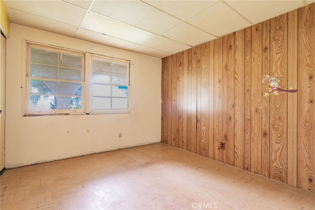 spare room with a drop ceiling and wood walls