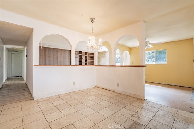 empty room with light tile patterned floors, ceiling fan with notable chandelier, and baseboards