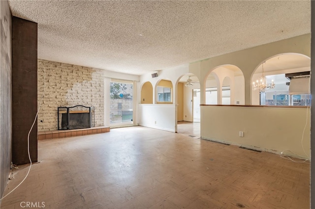 unfurnished living room featuring visible vents, arched walkways, a textured ceiling, a brick fireplace, and a notable chandelier