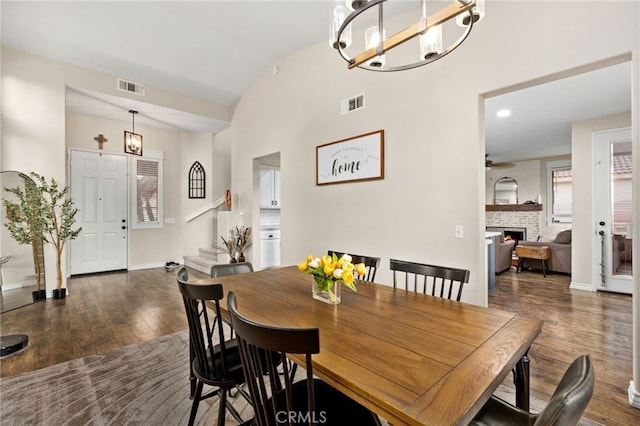 dining room with a notable chandelier, visible vents, a brick fireplace, and hardwood / wood-style flooring