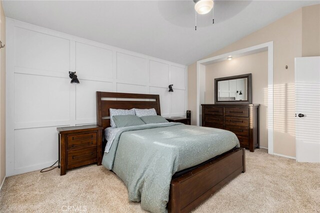 bedroom with vaulted ceiling, a decorative wall, light colored carpet, and ceiling fan