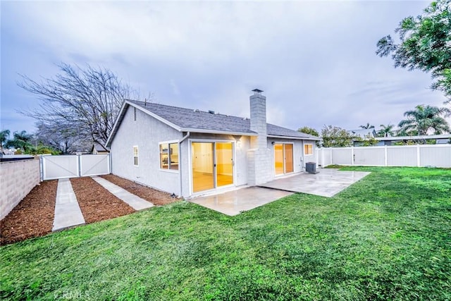 rear view of house with a gate, a fenced backyard, a chimney, a patio area, and a lawn