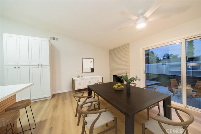 dining space with visible vents, a fireplace, light wood finished floors, ceiling fan, and vaulted ceiling