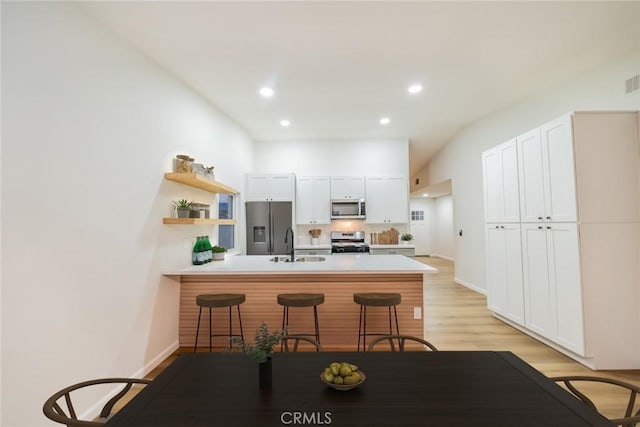 kitchen with a kitchen bar, a peninsula, white cabinets, stainless steel appliances, and a sink