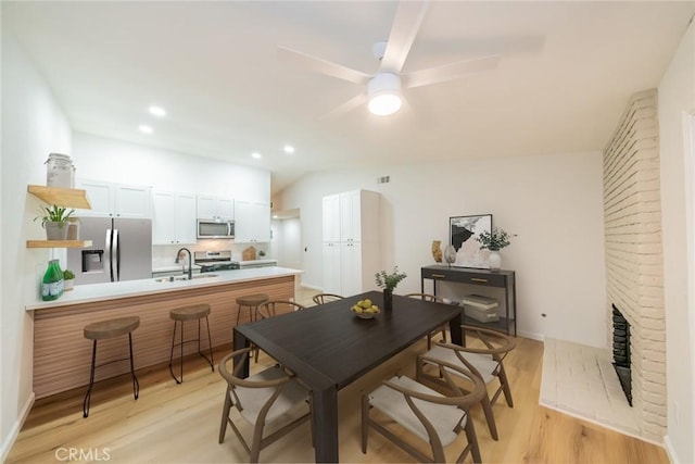 dining room featuring lofted ceiling, a brick fireplace, ceiling fan, and light wood finished floors