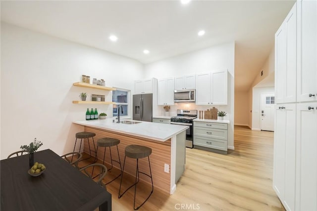 kitchen with a sink, a breakfast bar area, a peninsula, stainless steel appliances, and open shelves