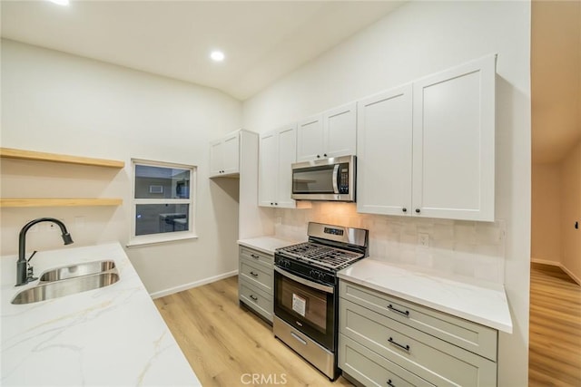 kitchen with light stone countertops, open shelves, a sink, appliances with stainless steel finishes, and backsplash