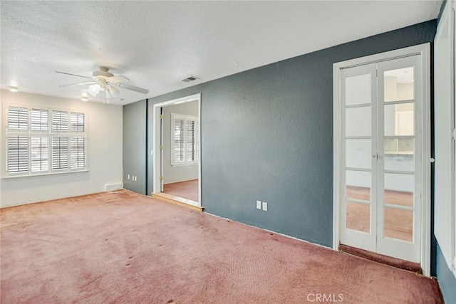 carpeted spare room with a ceiling fan, a textured wall, visible vents, and a textured ceiling