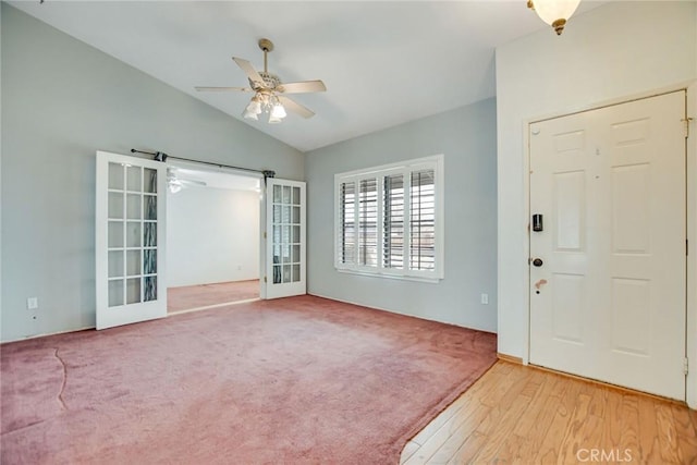 foyer entrance with a ceiling fan, lofted ceiling, light wood-style floors, french doors, and light carpet