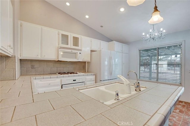 kitchen with white appliances, tile countertops, lofted ceiling, a sink, and white cabinetry