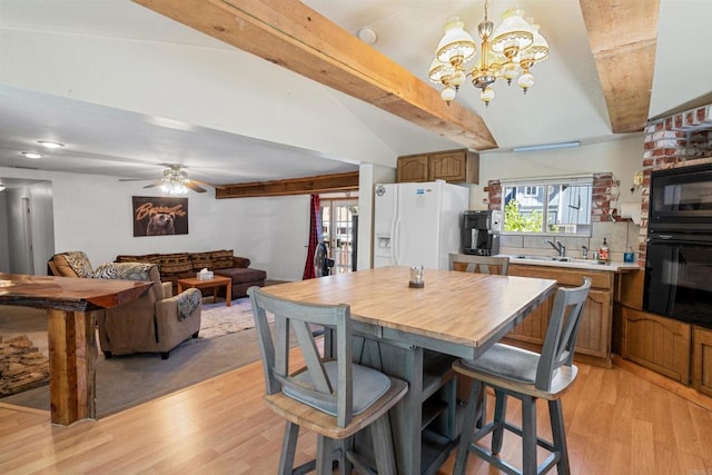 kitchen with light wood-type flooring, black appliances, a breakfast bar, decorative light fixtures, and vaulted ceiling with beams