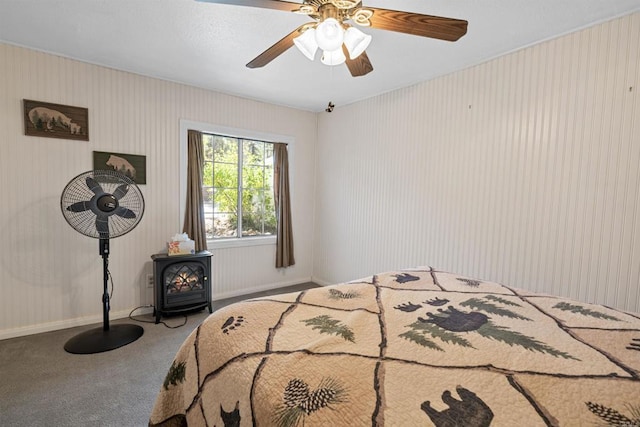 carpeted bedroom with a ceiling fan, a wood stove, and baseboards