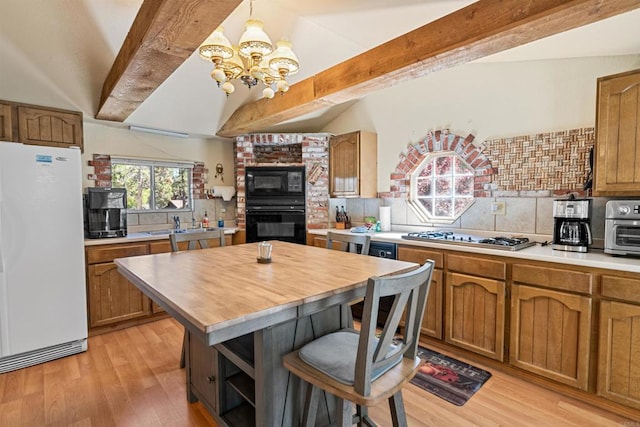 kitchen featuring beamed ceiling, black appliances, brown cabinetry, light wood finished floors, and decorative backsplash