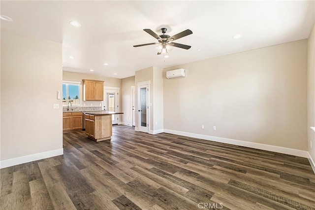 unfurnished living room featuring dark wood-type flooring, a wall mounted AC, a sink, baseboards, and ceiling fan