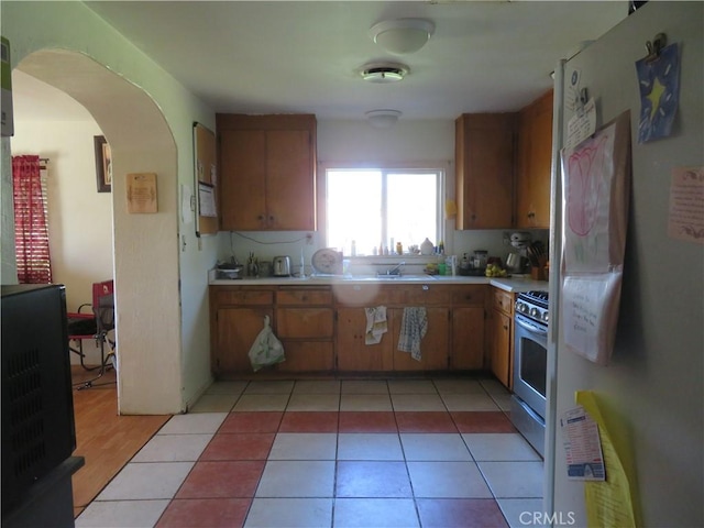 kitchen featuring stainless steel gas stove, freestanding refrigerator, arched walkways, light countertops, and light tile patterned floors