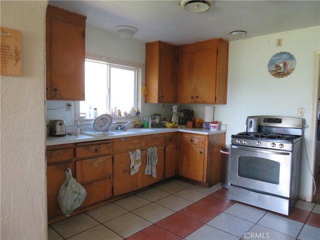 kitchen featuring stainless steel range with gas stovetop, brown cabinets, light countertops, and a sink