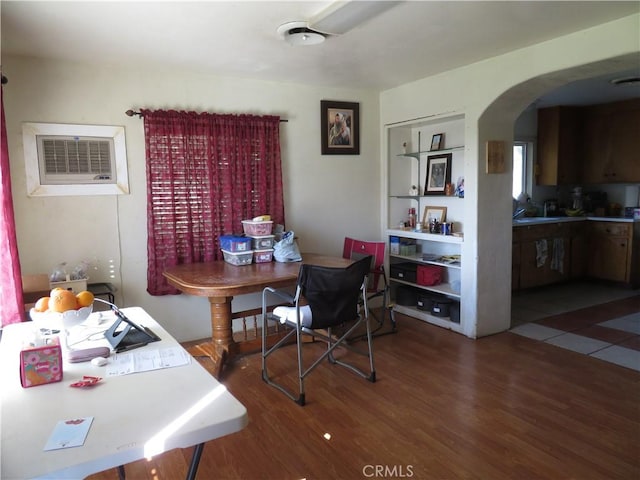 dining space with an AC wall unit, wood finished floors, and arched walkways