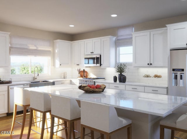 kitchen featuring a breakfast bar, a sink, stainless steel appliances, white cabinets, and a center island