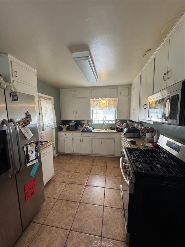 kitchen with light tile patterned flooring, white cabinetry, stainless steel appliances, and a sink