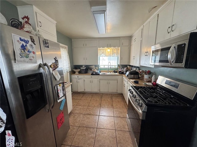 kitchen with a sink, stainless steel appliances, light tile patterned flooring, white cabinets, and light countertops