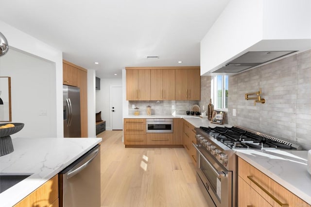 kitchen featuring light stone countertops, visible vents, stainless steel appliances, wall chimney range hood, and modern cabinets