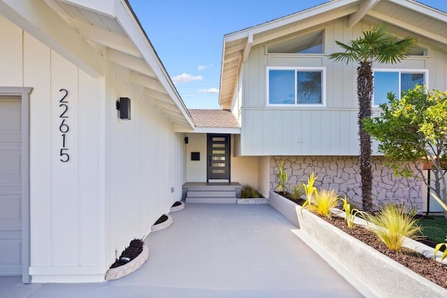 property entrance with board and batten siding, a garage, and a shingled roof