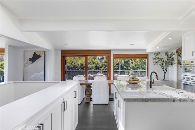 kitchen featuring a sink, dark wood-style floors, white cabinetry, double oven, and light stone countertops