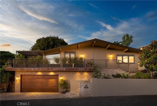 view of front of house with stucco siding, decorative driveway, a balcony, a garage, and brick siding