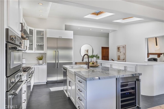 kitchen featuring dark wood-style floors, a center island with sink, wine cooler, glass insert cabinets, and high quality appliances