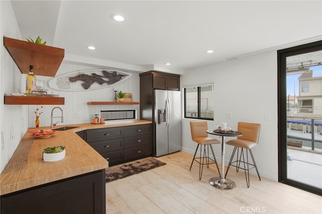 kitchen featuring open shelves, light countertops, stainless steel refrigerator with ice dispenser, and a sink