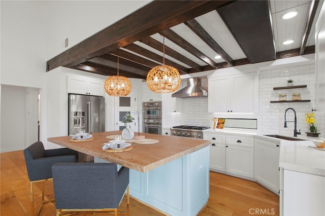 kitchen featuring open shelves, a sink, a center island, appliances with stainless steel finishes, and wall chimney range hood