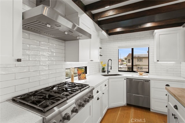 kitchen featuring stainless steel gas stovetop, light countertops, wall chimney range hood, and a sink