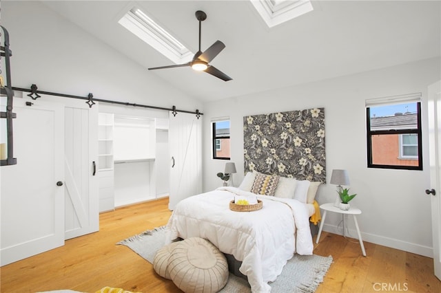 bedroom with vaulted ceiling with skylight, baseboards, a barn door, and wood finished floors