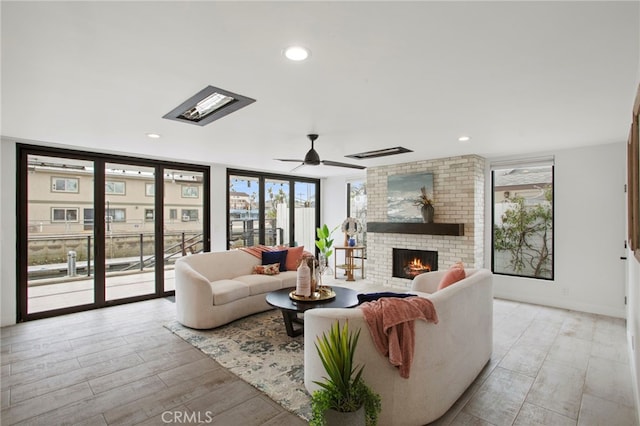 living room featuring plenty of natural light, light wood-style flooring, a brick fireplace, and a ceiling fan