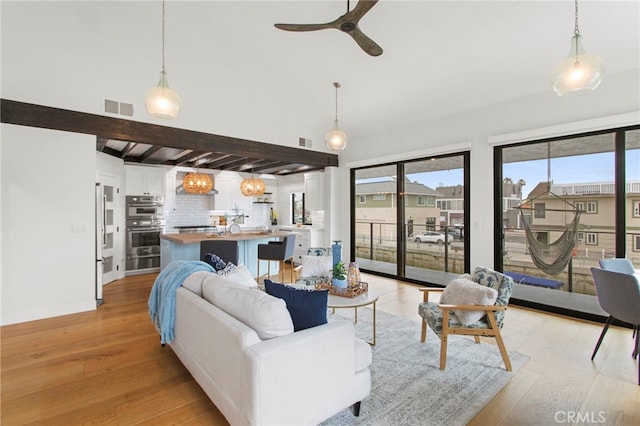 living area featuring beamed ceiling, light wood-style floors, visible vents, and ceiling fan