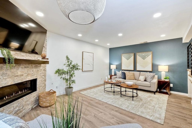 living room featuring a stone fireplace, recessed lighting, baseboards, and wood finished floors