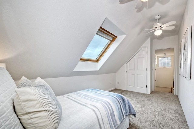 carpeted bedroom with vaulted ceiling with skylight and ceiling fan