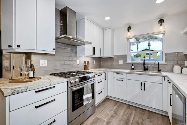 kitchen featuring a sink, appliances with stainless steel finishes, wall chimney exhaust hood, light wood-type flooring, and backsplash