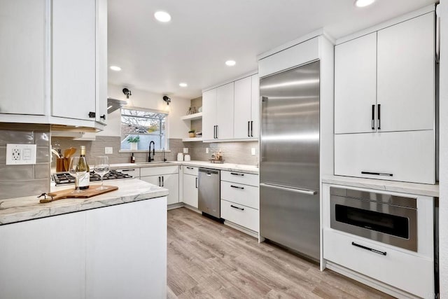 kitchen with light wood-type flooring, open shelves, a sink, tasteful backsplash, and built in appliances