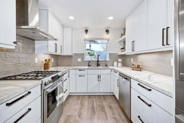 kitchen featuring a sink, light stone counters, white cabinetry, stainless steel appliances, and wall chimney exhaust hood