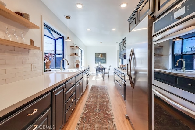 kitchen featuring light wood finished floors, tasteful backsplash, a sink, appliances with stainless steel finishes, and open shelves