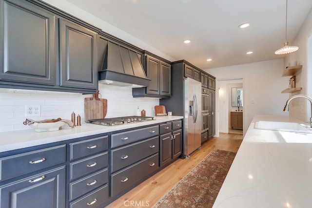 kitchen with premium range hood, light wood-type flooring, a sink, stainless steel appliances, and decorative backsplash