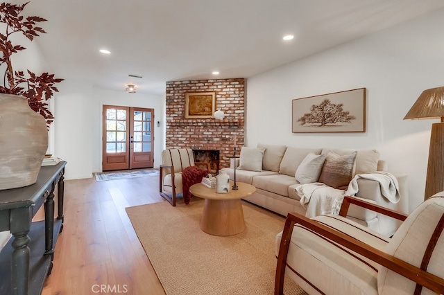 living room featuring light wood finished floors, visible vents, recessed lighting, a fireplace, and french doors